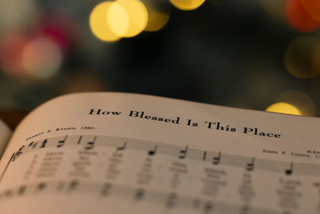 pexels-photo-29756510-29756510 Close-up of a hymn book page with 'How Blessed Is This Place' amidst warm bokeh lights.